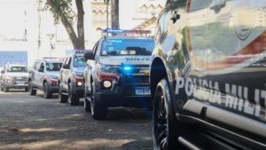 suspeito de manter o ex-sogro em cárcere privado: Viaturas policiais em fila na rua durante uma ocorrência em Mogi Guaçu, com foco em um carro da polícia com luzes azuis no patrulhamento.