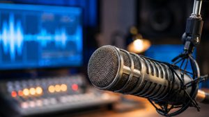 Rádio 3.0 em estúdio de rádio, com microfone de metal em primeiro plano diante de equipamentos e luzes desfocadas ao fundo, sugerindo transformação em andamento.