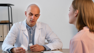 Médico conversa com paciente em consultório enquanto analisa caixas e frascos de remédio, ilustrando novo medicamento para doenças autoinflamatórias aprovado pela Anvisa.