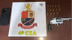 homem agride companheira grávida: Placa com o texto “4ª CIA” e brasão de unidade policial ao lado de um revólver apreendido, em imagem ligada a prisão em Hortolândia.