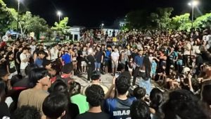 Prefeito veta campeonato farmar aura: Multidão reunida ao ar livre à noite em uma cidade do litoral de SP, em meio a um evento cercado por espectadores, com foco em reação popular e debate sobre a decisão do prefeito que veta campeonato de “farmar aura”.