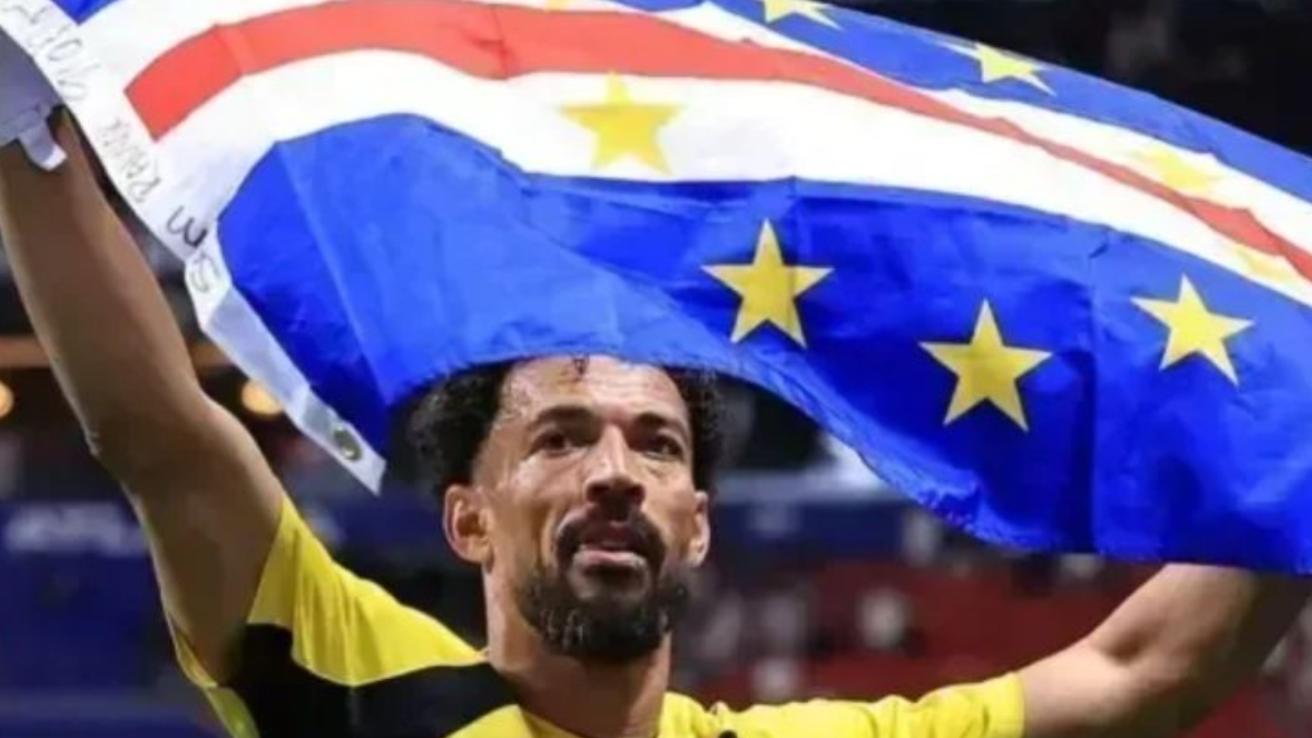 Bandeira azul com estrelas e faixa amarela sobre o rosto de um jogador de futebol ao fundo em estádio, com expressão de celebração e uniforme amarelo; contexto de destaque sobre Vozinha no Colo-Colo.
