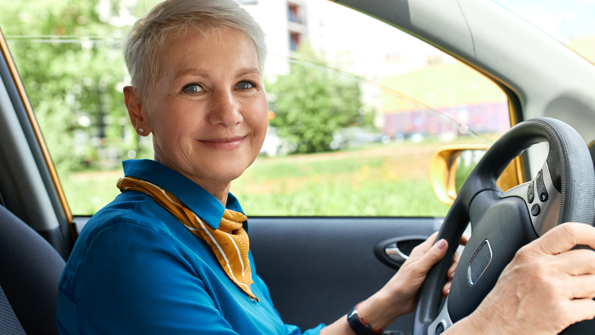 Idosa ao volante dentro do carro, pronta para dirigir, em imagem que destaca a Credencial de estacionamento para idosos e a emissão online gratuita.