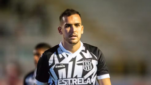 Ponte transfer ban: Jogador de futebol em campo usando uniforme do Ponte Preta, com escudo do clube na camisa, em imagem desfocada ao fundo, relacionada a uma crise envolvendo transfer ban da FIFA.