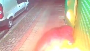 Fogo papelaria Praia Grande: Fogo e fumaça saindo da entrada de uma papelaria no litoral de SP, com carros estacionados na rua, em uma cena de tentativa de incêndio registrada em vídeo.