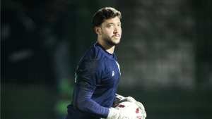 Caíque França, goleiro do Guarani, em campo usando uniforme azul e luvas de goleiro durante partida, com fundo desfocado do estádio.