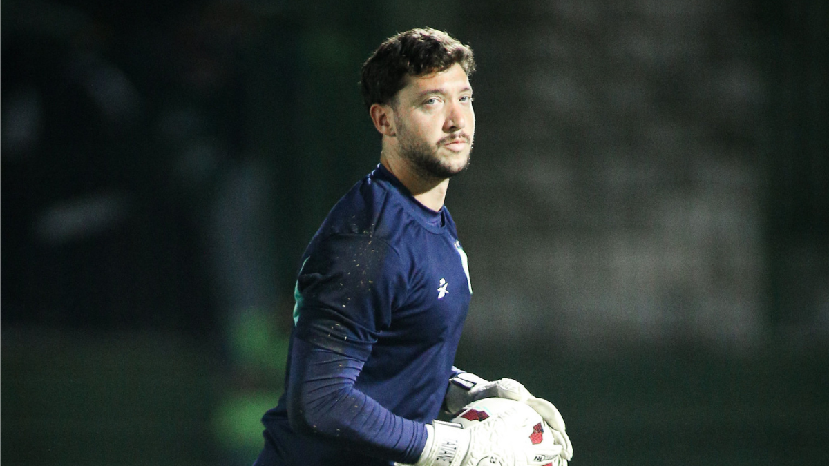 Caíque França, goleiro do Guarani, em campo usando uniforme azul e luvas de goleiro durante partida, com fundo desfocado do estádio.