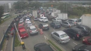 Caos no litoral: ventania suspende temporariamente travessias de balsas, enquanto há intenso congestionamento na estrada com filas de veículos e caminhões.