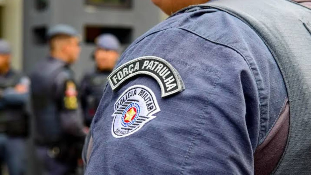 Homem com uniforme da Força Patrulhada da Polícia Militar, com o emblema “Força a Patrulha” e “Polícia Militar”, ao fundo há agentes em patrulhamento; Sumaré reduz criminalidade e registra queda nos índices de violência em SP.