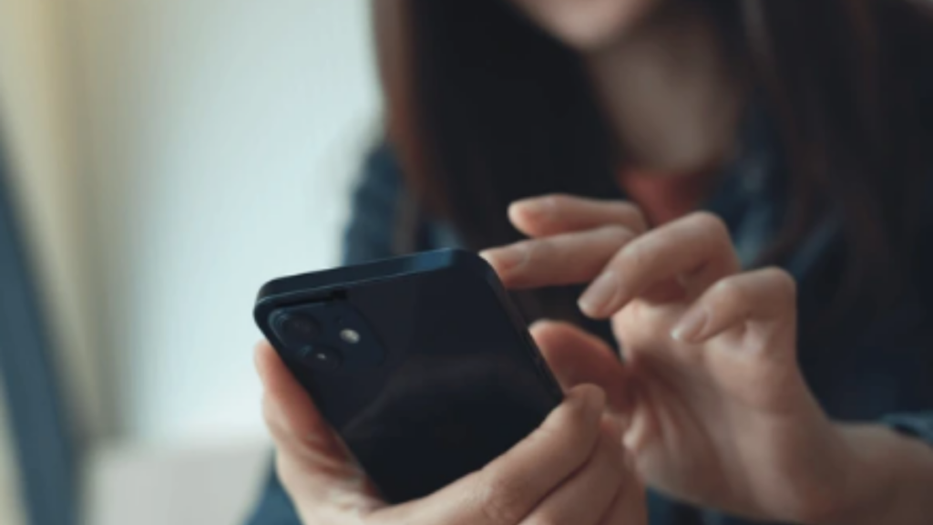 Pessoa segura um celular na mão, com foco em um dispositivo móvel usado para acessar serviços de segurança e canais de denúncia, em contexto de novas regras de proteção às mulheres após sanção do Governo Federal.