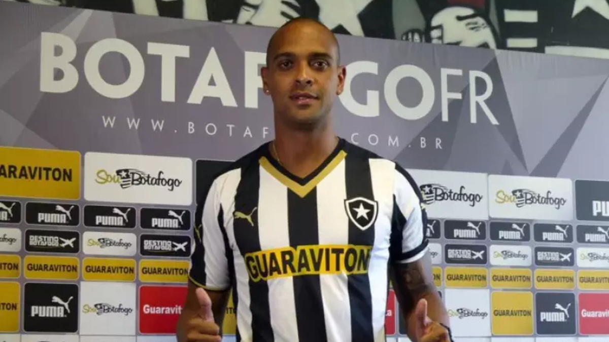 Tássio ex-botafogo em coletiva de imprensa do Botafogo, usando uniforme listrado preto e branco e posando em frente a um painel com patrocinadores no Rio de Janeiro.