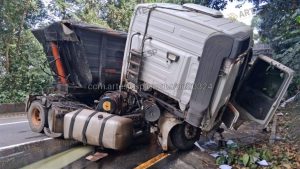 Anchieta tem congestionamento após carreta perder freios em Cubatão: caminhão de carga tombado na pista, com motor e compartimento da cabine danificados, trânsito lento ao fundo.