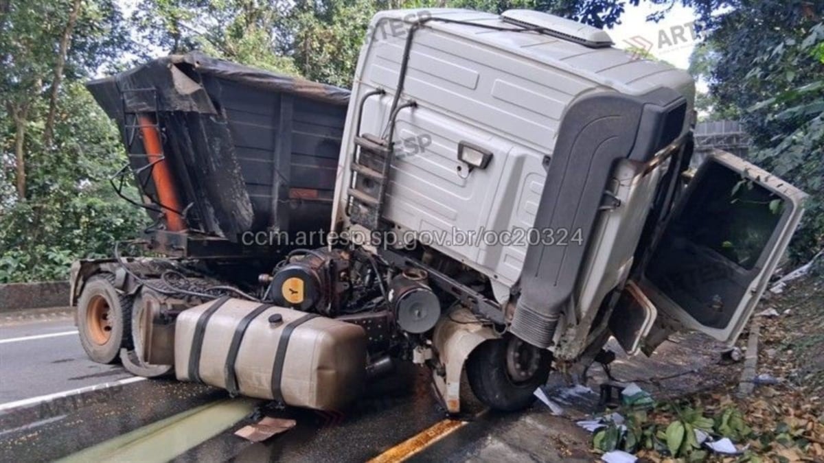 Anchieta tem congestionamento após carreta perder freios em Cubatão: caminhão de carga tombado na pista, com motor e compartimento da cabine danificados, trânsito lento ao fundo.