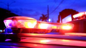 Luzes de giro de viatura policial em cena noturna, enquanto trabalhadores investigam uma granada encontrada em Socorro em loteamento, com viaturas ao fundo.