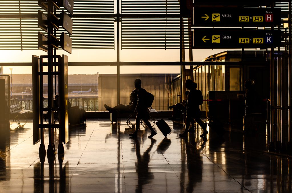 Passageiros com malas em um saguão de aeroporto ao pôr do sol, com placas de embarque e visão do terminal; Receita Federal agiliza desembarque com novo sistema automatizado.