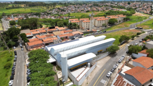 Contratação de médicos em Campinas: Vista aérea de um hospital da Rede Mário Gatti em Campinas, com prédio e estacionamentos ao lado da estrada, divulgando abertura de inscrições para seleção de médicos.