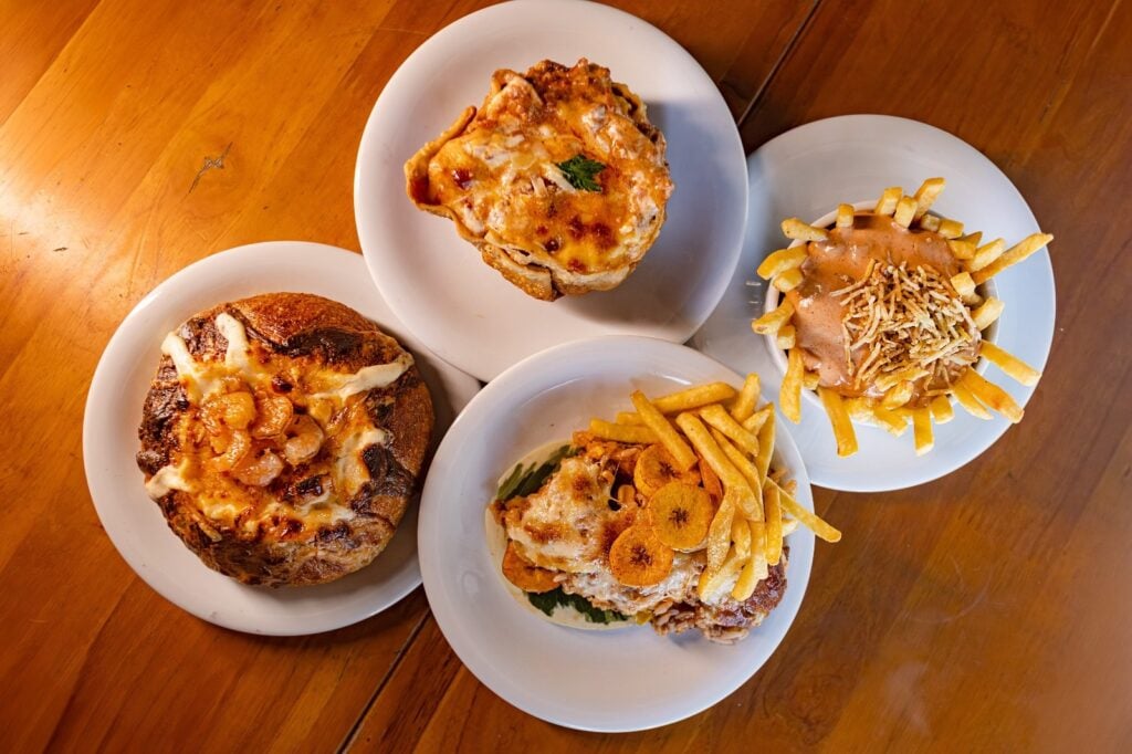 Piracicaba: pratos de comida servidos em tigelas e pratos brancos sobre mesa de madeira, com pizzas e porções como batatas e carne com queijo, no 8º Festival Gastronômico Comida na Rua.