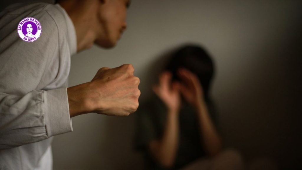 Ilustração com um homem levantando o punho e uma mulher ao fundo com as mãos no rosto, criando um alerta sobre violência contra a mulher e suas formas iniciais. Texto: “Ele não vai começar te dando um soco”: as cinco caras da violência contra a mulher.