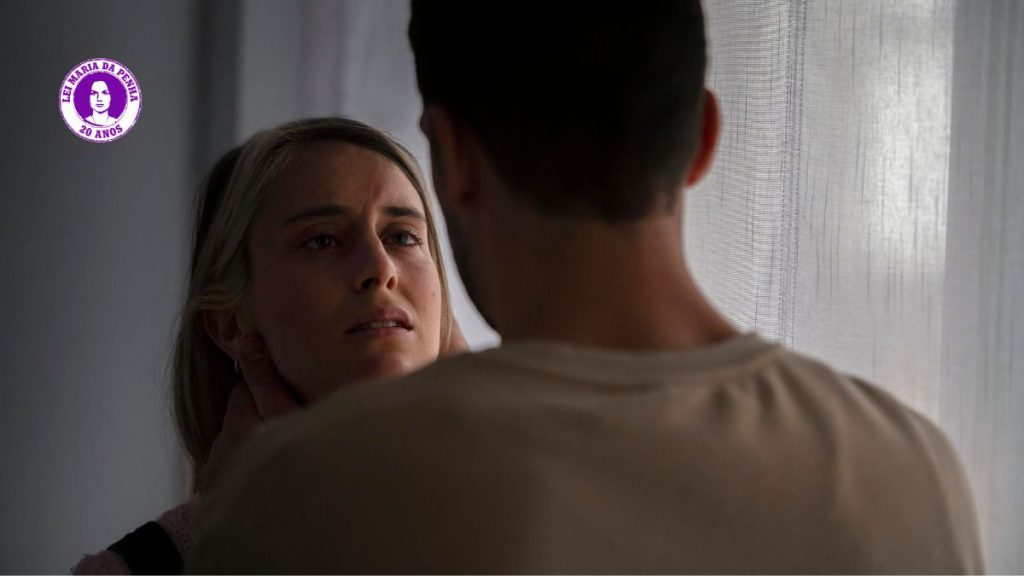 Imagem com alerta sobre violência contra a mulher, com uma mulher em primeiro plano olhando para um homem em cena doméstica; texto “Ele não vai começar te dando um soco” e “as cinco caras da violência contra a mulher”.