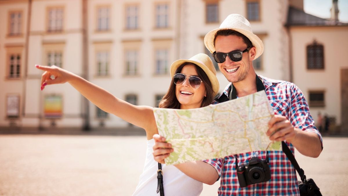 Casal de turistas com chapéus e mapa, em viagem turística no centro de uma cidade, destacando faturamento do turismo com movimentação de R$ 23,2 bilhões em maio de 2026.