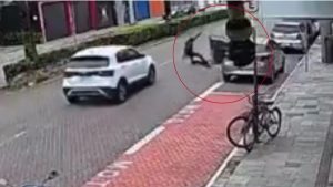 Vídeo de segurança mostra jovem de patinete atropelado em Praia Grandemar após ser derrubado por uma porta de carro, em uma rua movimentada.