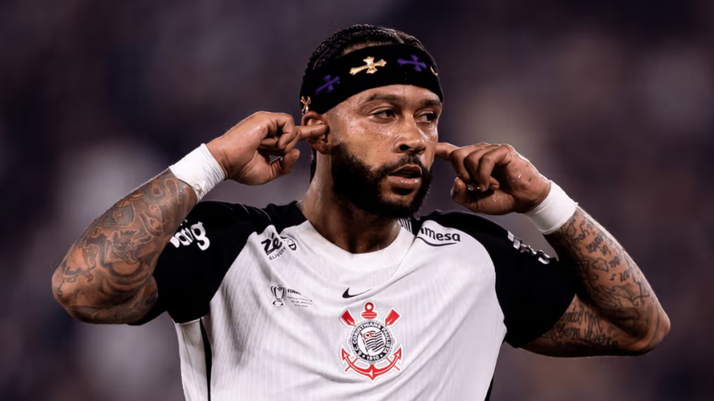 Memphis comemora gol pelo Corinthians, em foto de Rodrigo Coca pela Agência Corinthians, com o jogador de uniforme branco fazendo gesto de comemoração no estádio.