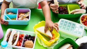 Volta às aulas: crianças montam lanches saudáveis na lancheira, com sanduíches, frutas e legumes separados em potes coloridos