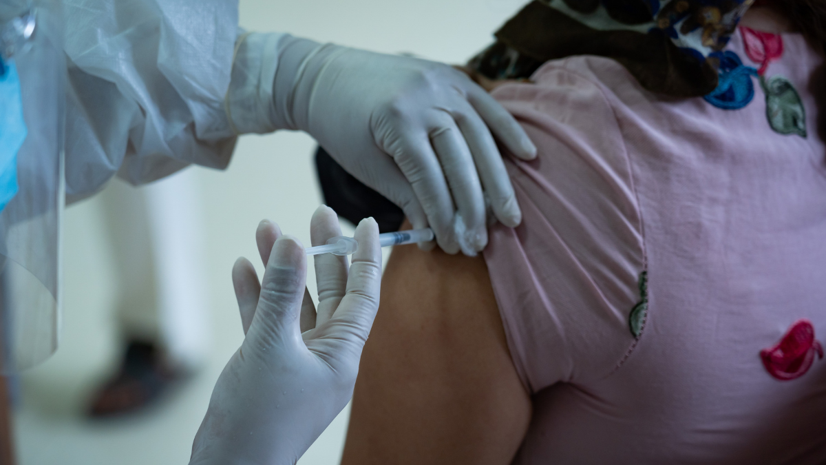 Profissional de saúde usando luvas aplica vacina no braço de uma pessoa, em cenário que remete a prevenção e informações sobre gripe, com foco em aumento de óbitos por influenza.