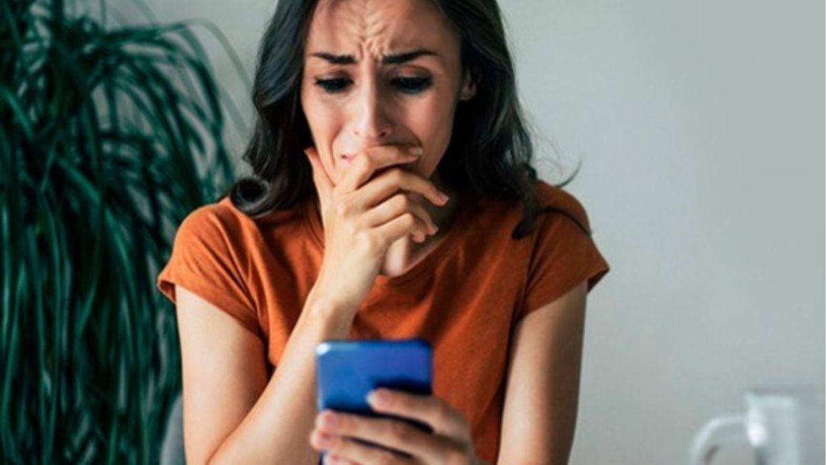 Mulher com expressão preocupada, segurando um celular na sala de estar, em cena que destaca a necessidade de medida protetiva lei maria da penha para transformar proteção em segurança real após anos de desafios.