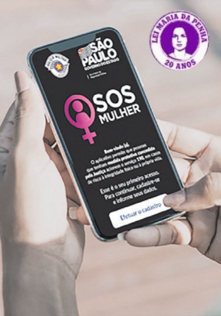 Representação dos 20 anos da Lei Maria da Penha. Uma mulher segurando um celular com a tela inicial do aplicativo SOS Mulher, para efetuar o cadastro.