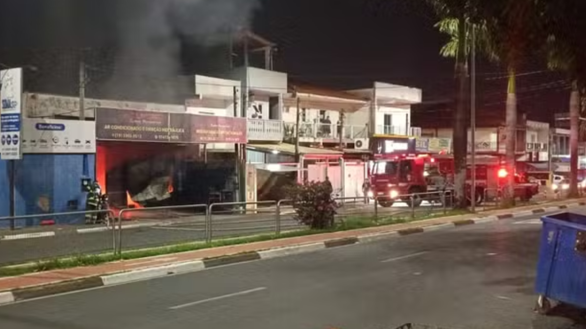 incêndio em oficina de Hortolândia: equipes de bombeiros e viaturas em frente a um galpão com fumaça e chamas, veículos destruídos e área isolada à noite.