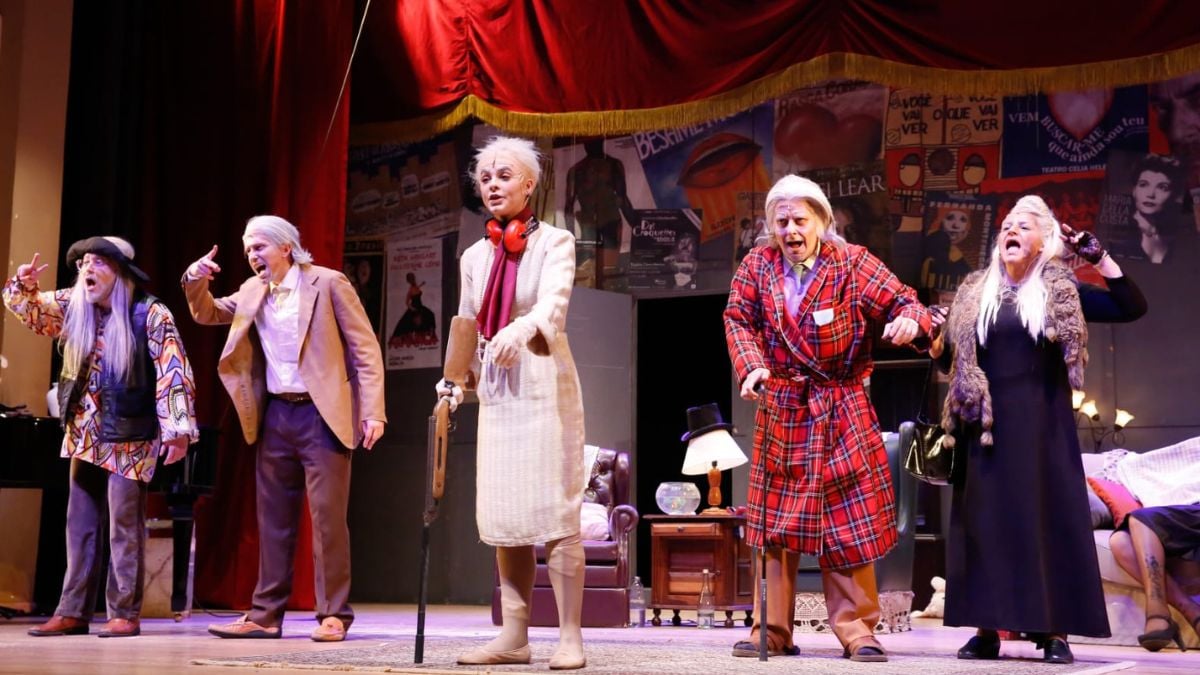 Musical Forever Young em cena: atores encenam com figurinos coloridos em um palco, com cenário temático ao fundo e iluminação de teatro. Carmo Dalla Vecchia e Vanessa Gerbelli se apresentam.