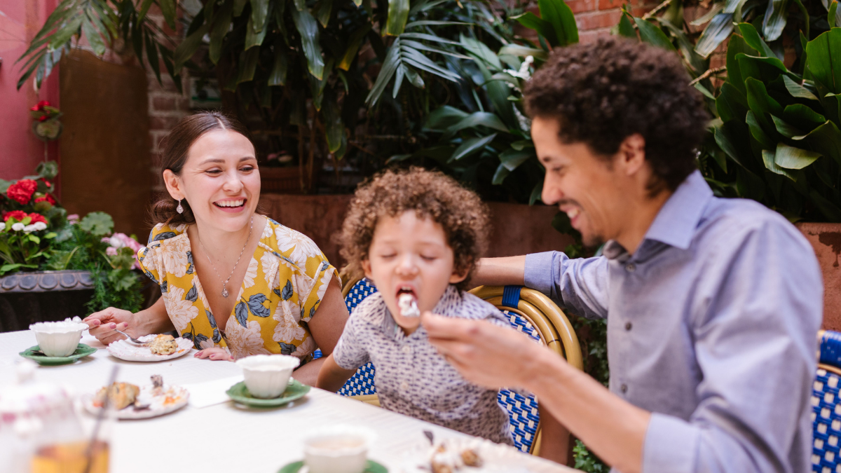 No Dia dos pais, família reunida em um almoço em restaurante: pai alimenta uma criança à mesa com pratos e bebidas ao ar livre em Campinas e Araras.