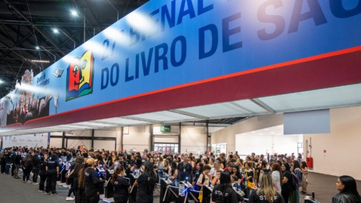 Bienal do Livro terá maior edição da história e ingresso com cashback total em foto de público reunido em área de estande, com banner “Dia do Livro” ao fundo em evento.