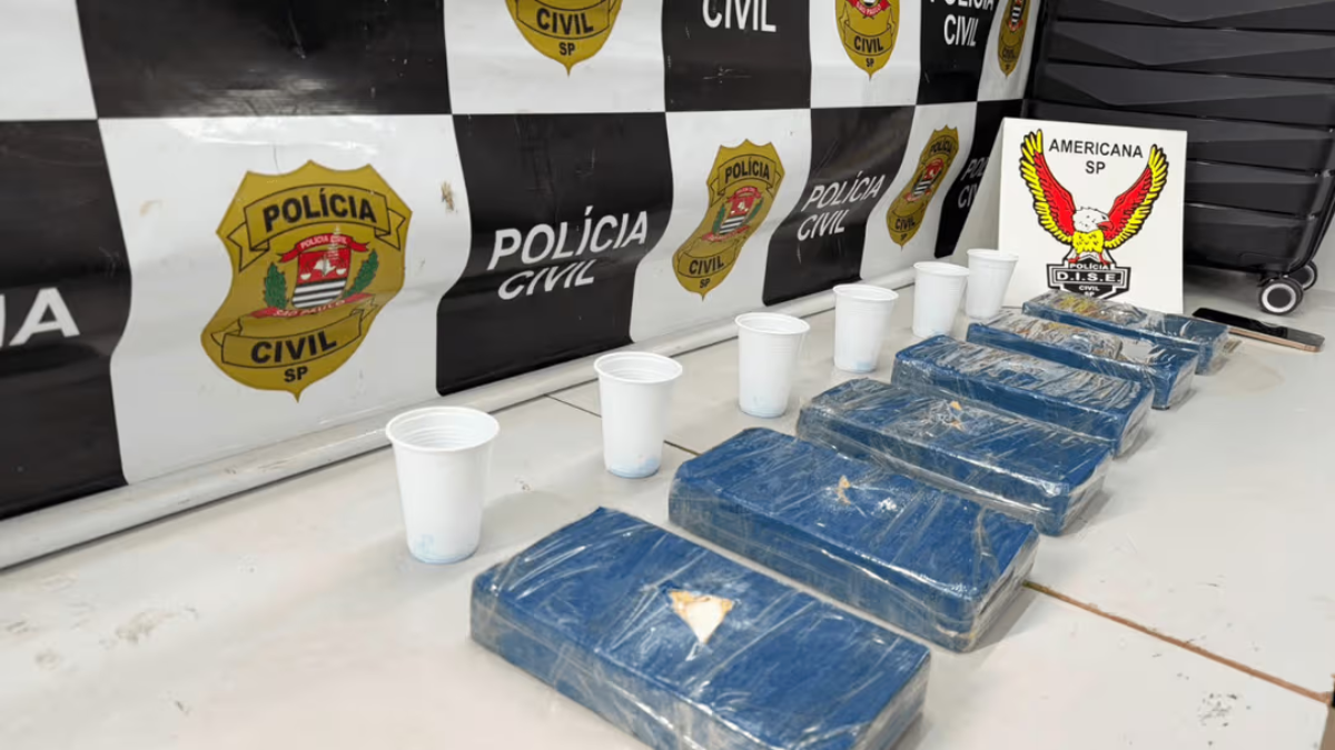 mulher presa com 6 kg de cocaína: Operação da Polícia Civil em Americana: embalagens com cerca de 6,2 kg de cocaína apreendidos, exibidos em mesas com copos plásticos e fundo com insígnias da Polícia Civil SP.