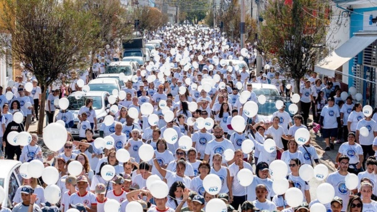 Caminhada pela Paz Amparo: Caminhada pela Paz em Amparo com participantes em massa usando camisetas brancas e balões brancos em uma avenida, sugerindo atividades gratuitas de saúde, cultura e meio ambiente.
