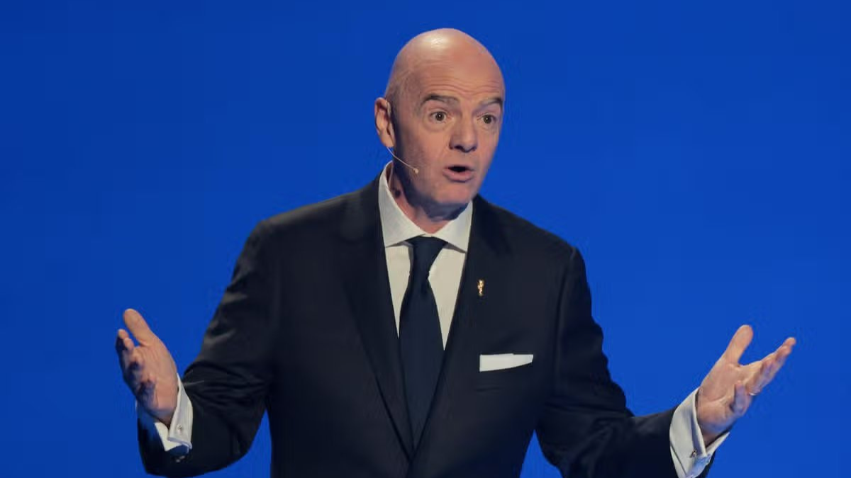 Uefa em destaque em um homem de terno com microfone de apresentador, em cenário azul, sugerindo fala oficial sobre FIFA e ameaça de boicote à Copa do Mundo.