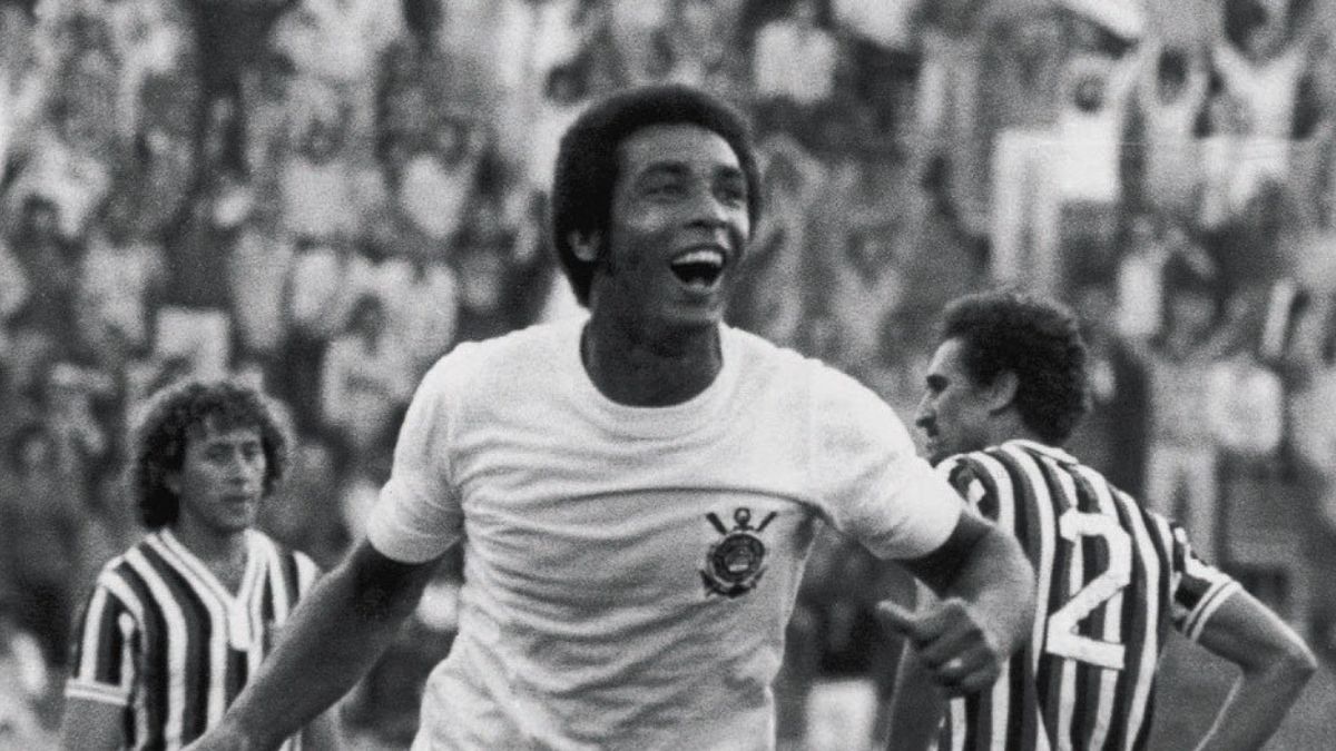 Geraldão, ídolo do Corinthians, aparece em foto em preto e branco em campo durante partida contra o Santos, marcado no centro em pose de comemoração com torcidas ao fundo.