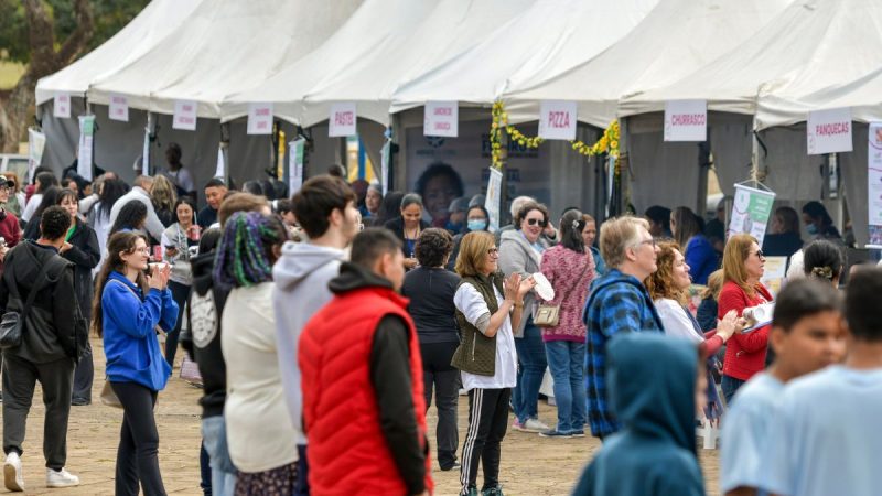Movimentação de pessoas em tendas brancas durante a Feira Conexão Social em Campinas, com público reunido para projetos sociais e programação cultural ao ar livre.