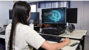 curso gratuito em São Vicente: Pessoa com fone de ouvido trabalhando em computador em laboratório, com tela exibindo informações sobre curso de inteligência artificial e tema de IA Generativa, em contexto de treinamento profissional