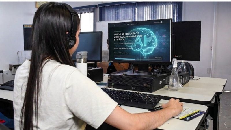 curso gratuito em São Vicente: Pessoa com fone de ouvido trabalhando em computador em laboratório, com tela exibindo informações sobre curso de inteligência artificial e tema de IA Generativa, em contexto de treinamento profissional