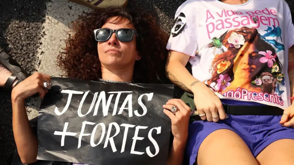 Manifestação com cartaz escrito “JUNTAS + FORTES” e pessoas ao ar livre, em referência a 20 anos da Lei Maria da Penha e aos desafios dos próximos 20 anos começam hoje.