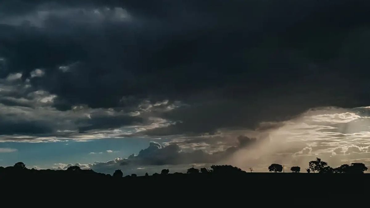 Alerta do Inmet: entenda o que significam as cores amarela, laranja e vermelha em avisos meteorológicos, com céu nublado e tempestade ao fundo.