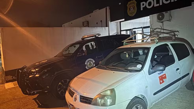 Falsos funcionários de telefonia: dupla suspeita em viaturas da polícia, em Santa Bárbara, após furto de cabos, com carro branco e viatura ao fundo.