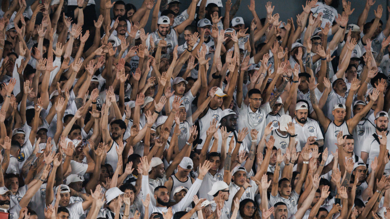 santos x athletico-pr: Torcida do Santos lota as arquibancadas e protesta após derrota para o Athletico, com mãos erguidas e expressões de indignação, xingando o presidente.