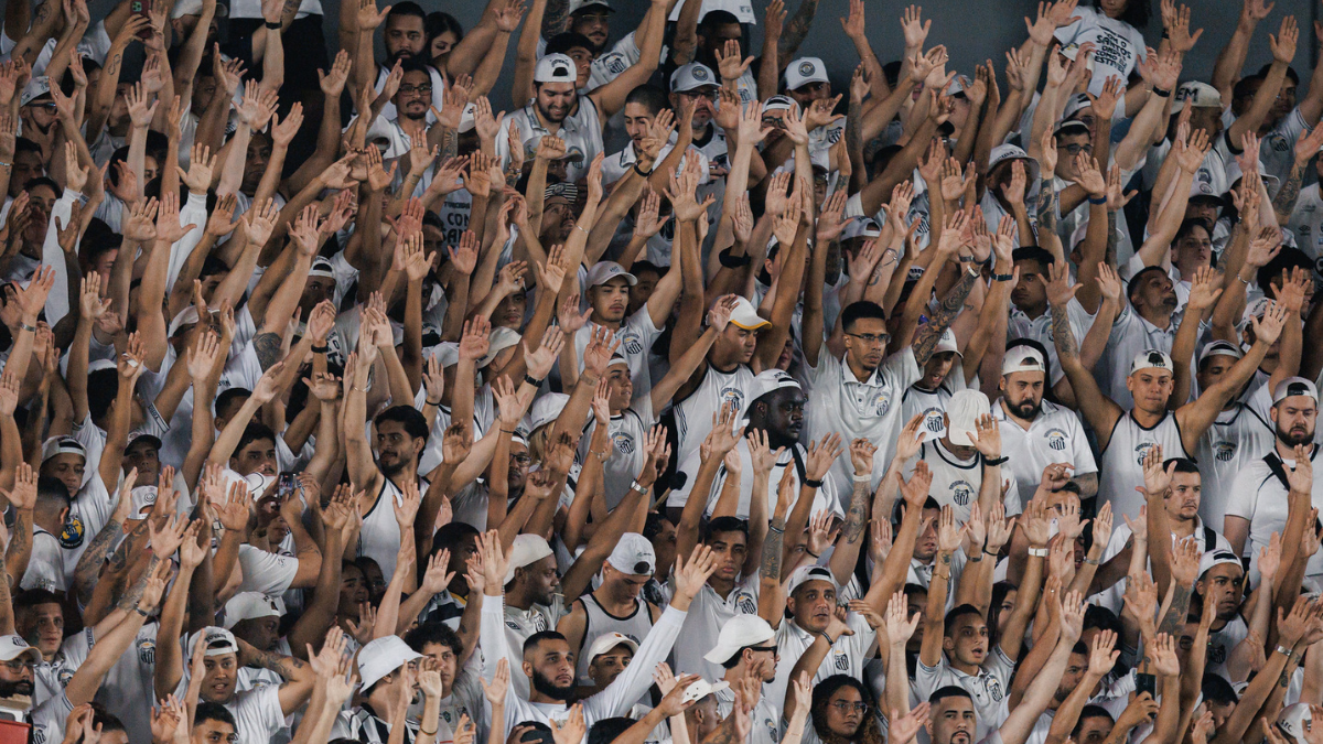 santos x athletico-pr: Torcida do Santos lota as arquibancadas e protesta após derrota para o Athletico, com mãos erguidas e expressões de indignação, xingando o presidente.