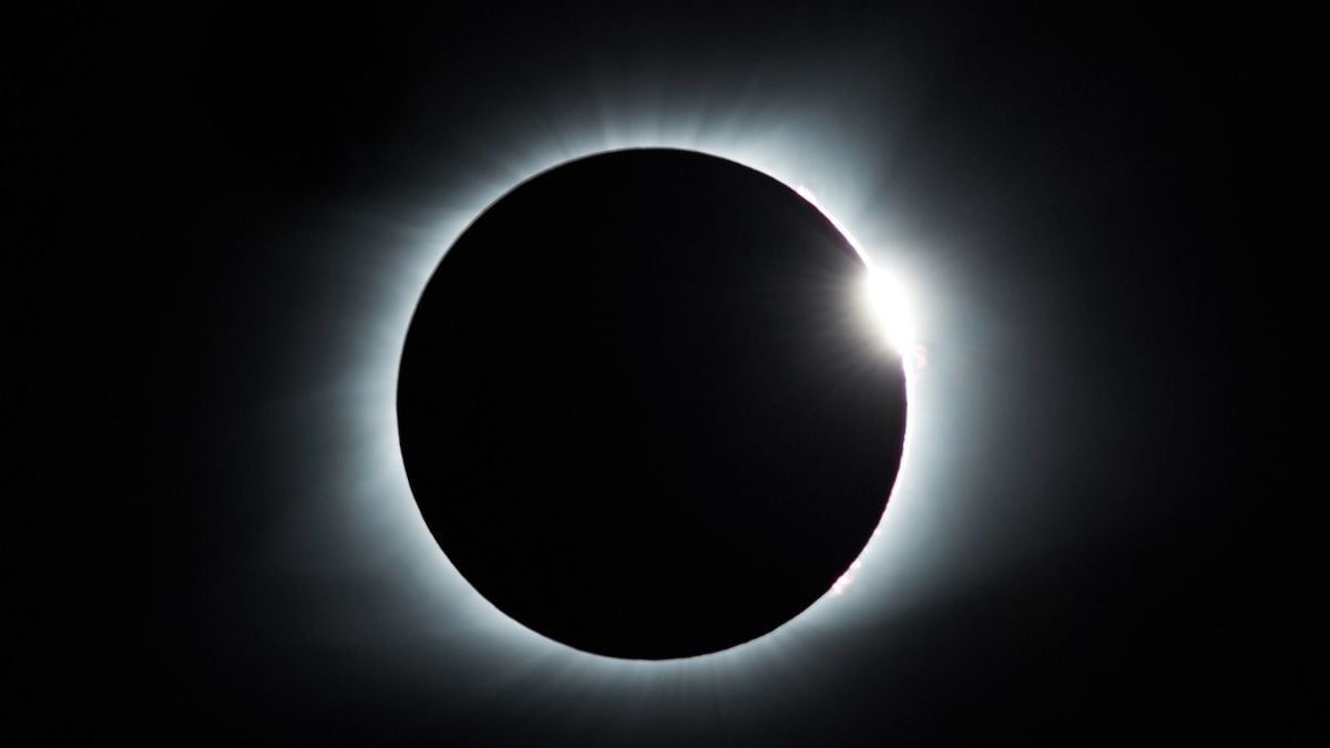 Eclipse solar em agosto, com o disco escuro da Lua cobrindo parcialmente o Sol e um halo luminoso ao redor no céu noturno.