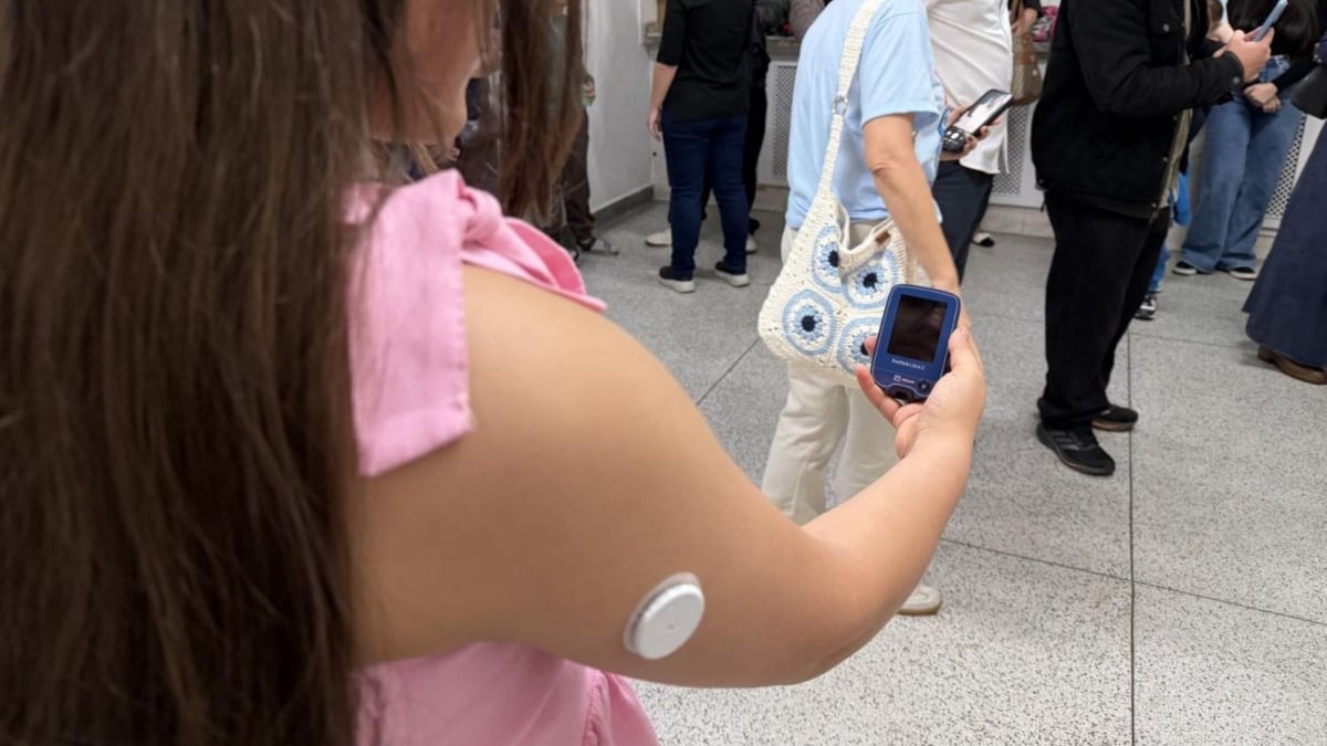 Foto de uma criança usando um dispositivo de monitoramento com visor na mão e um sensor fixado no braço, em ação de entrega de sensores de glicose para acompanhar o diabetes infantil em Indaiatuba.
