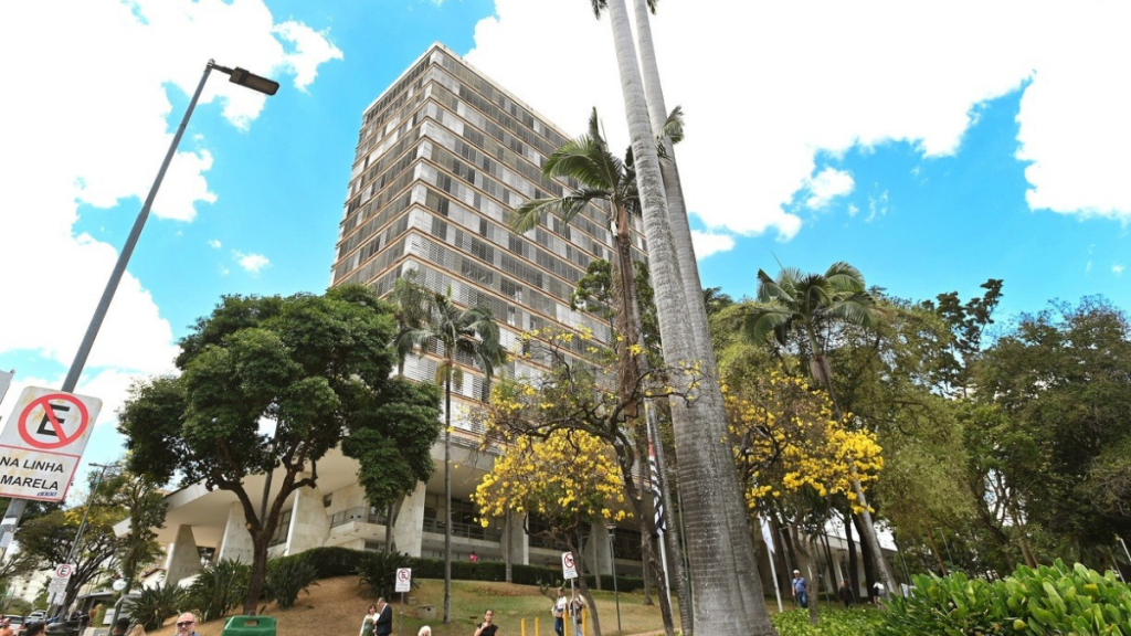 Feriado em Campinas impacta serviços municipais: prédio público e palmeiras em frente à paisagem urbana, com céu azul e placa de sinalização de trânsito