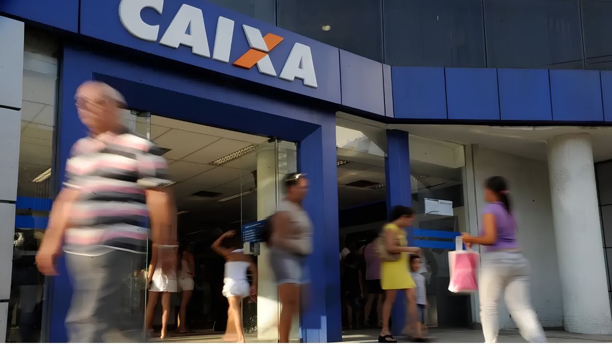 mega-sena dia dos pais: Pessoas passam em frente a uma fachada da Caixa em uma imagem noturna, com placas e movimento de pedestres ao redor da entrada do banco. Mega-Sena: quatro apostas da Baixada Santista acertam a quina no Dia dos Pais.